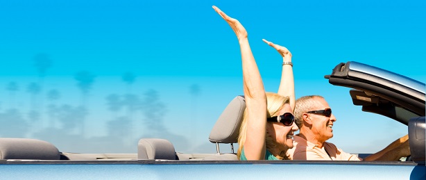 Happy older couple in convertible with hands raised