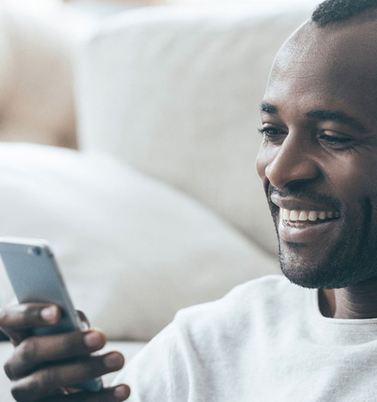 A man sitting on a couch smiling at his phone.