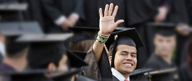 A young man in graduation gown waving towards the camera.